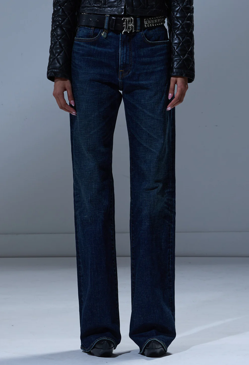 Person wearing dark blue jeans and a black jacket on a plain background