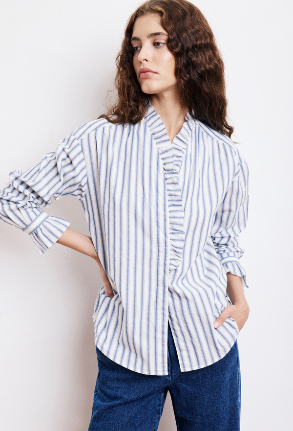 Woman wearing a blue and white striped shirt with a ruffled collar against a plain background