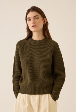 Woman wearing a muddy green sweater against a beige background