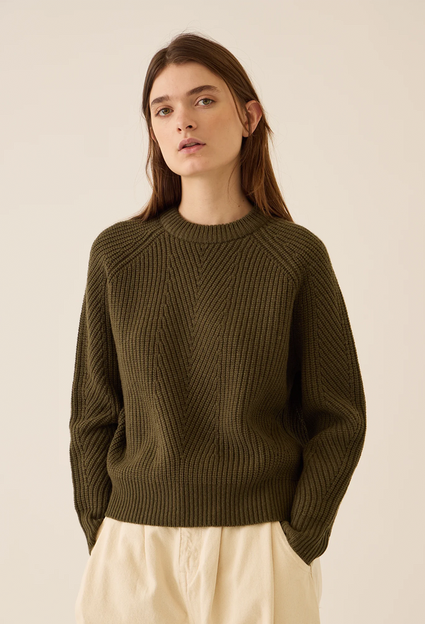 Woman wearing a muddy green sweater against a beige background