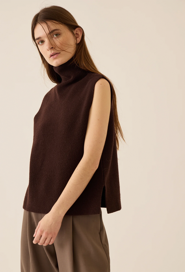 Woman wearing a brown sweater vest and beige pants against a beige background