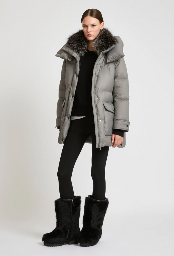 Woman wearing a gray winter coat with fur trim and black boots on a white background