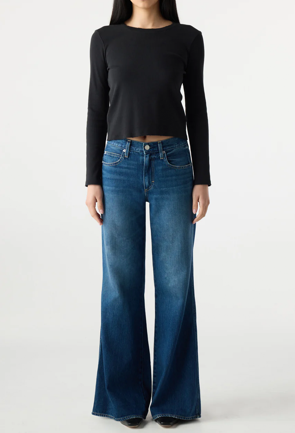 Person wearing a black long-sleeve top and blue flared jeans on a white background