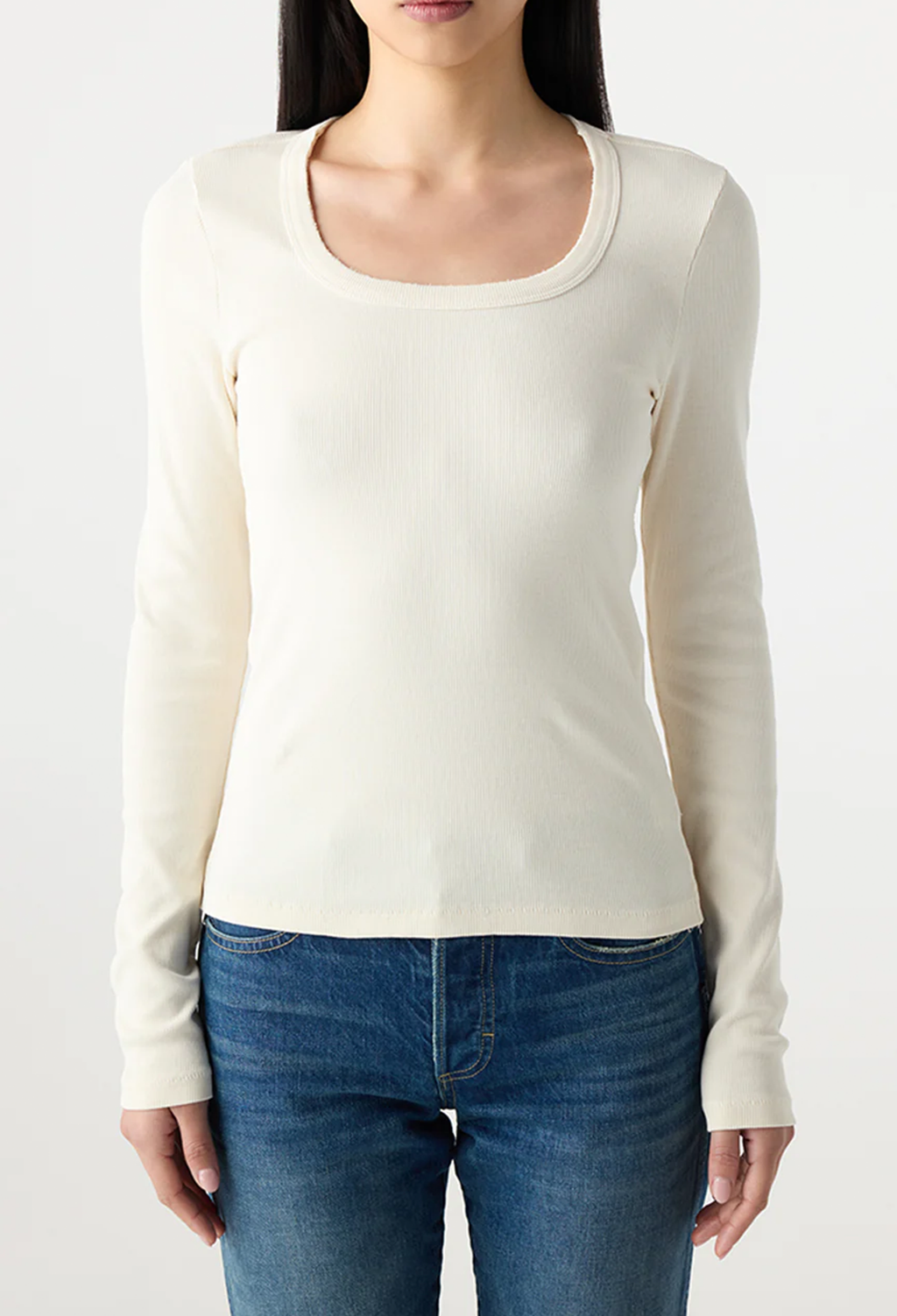 Woman wearing a white long-sleeve top and blue jeans on a plain background