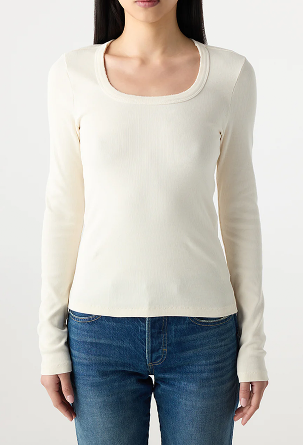 Woman wearing a white long-sleeve top and blue jeans on a plain background
