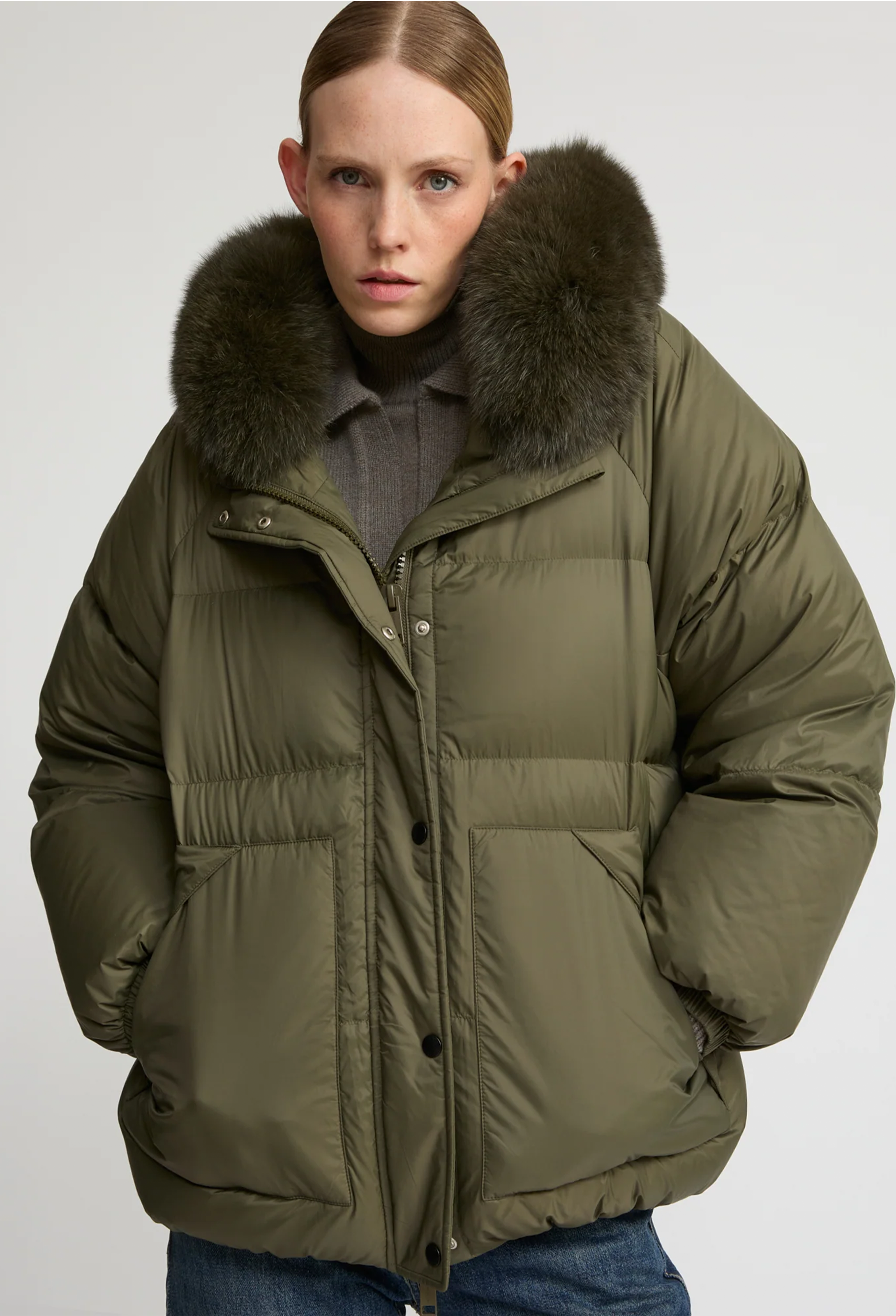 Person wearing a green puffer jacket with a fur-lined hood on a white background