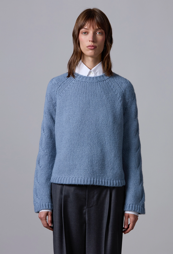 Woman wearing a blue sweater over a white shirt with a gray background