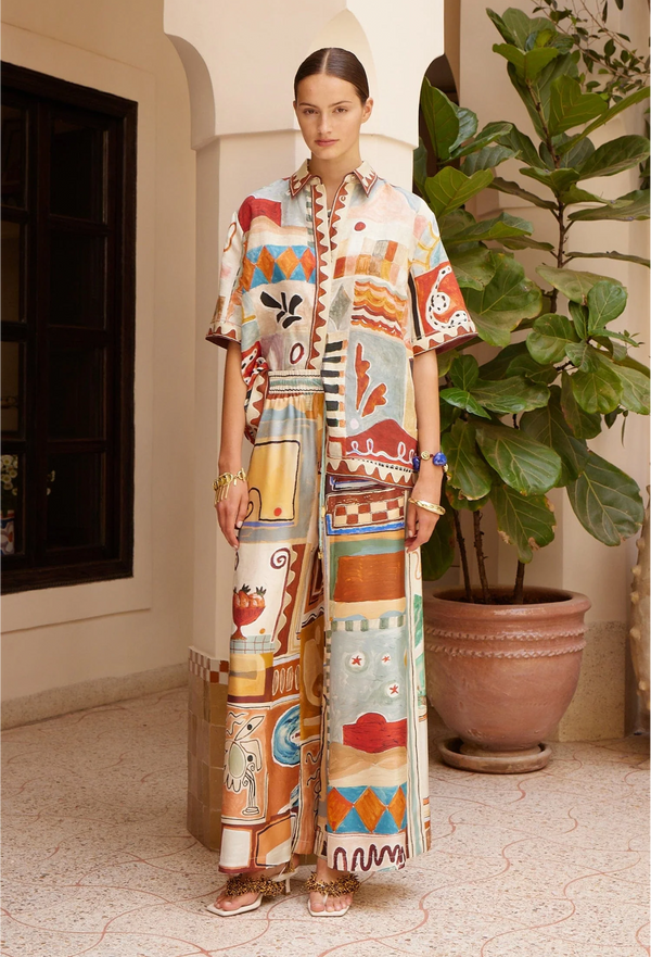 Woman wearing a colorful patterned outfit standing indoors with a plant in the background