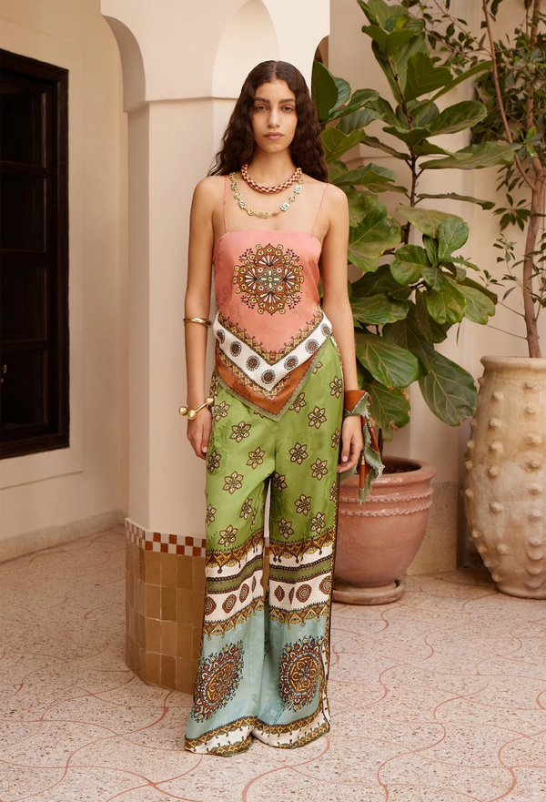 Woman in a colorful outfit standing in an outdoor setting with plants and a column.