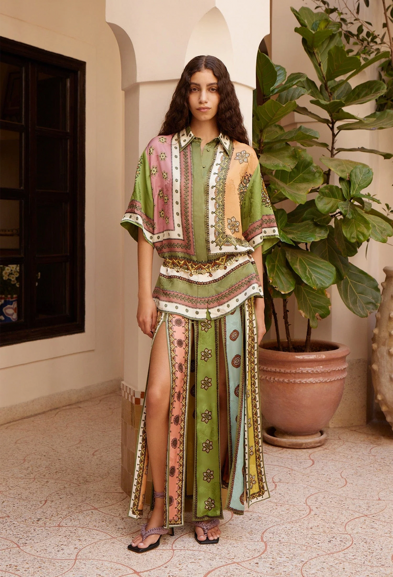 Woman wearing a patterned outfit standing in a room with a plant.