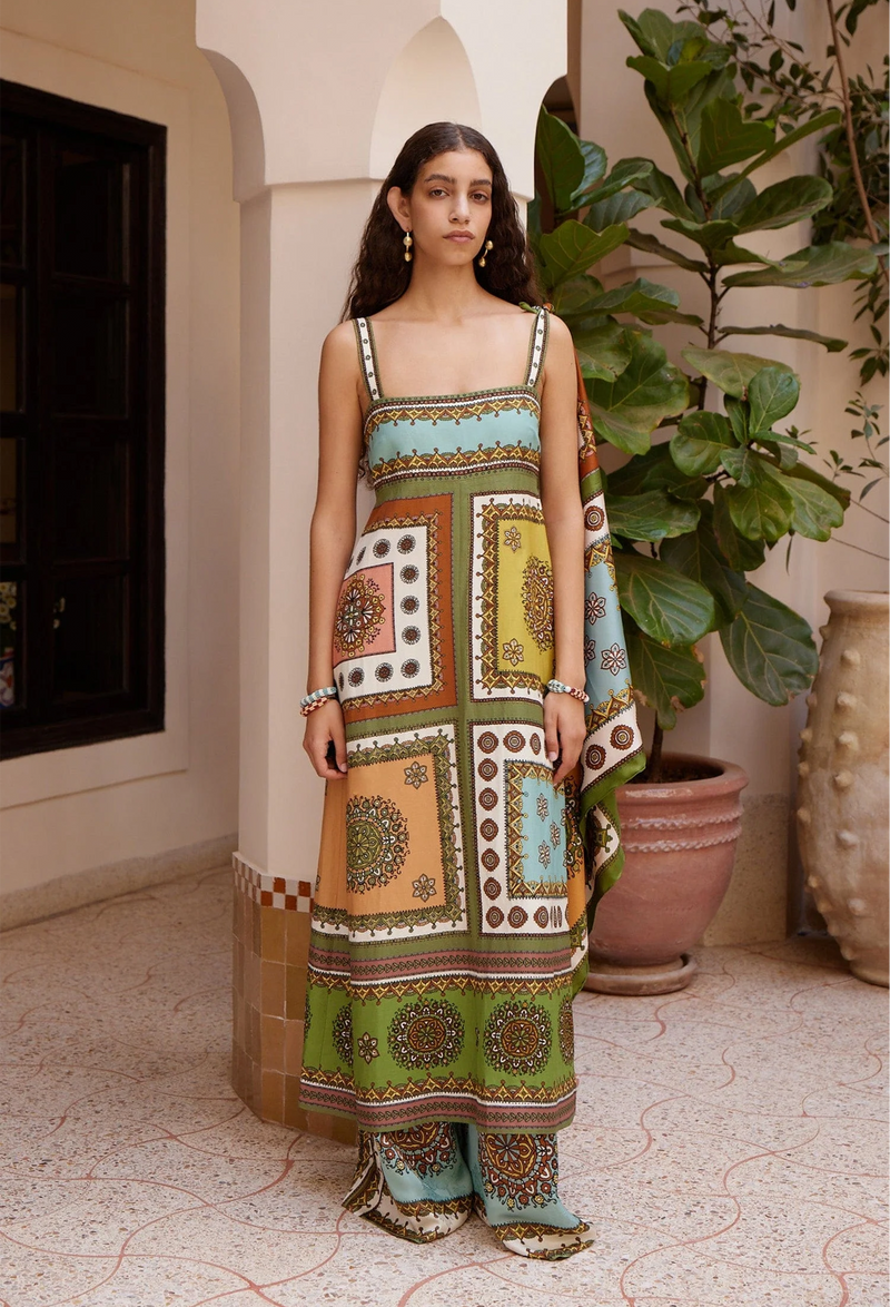 Woman wearing a colorful patterned dress standing in a decorative indoor setting with plants.