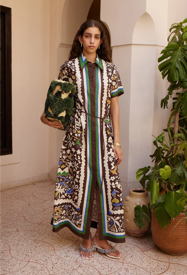 Woman in a patterned dress holding a green bag in an outdoor setting with plants.