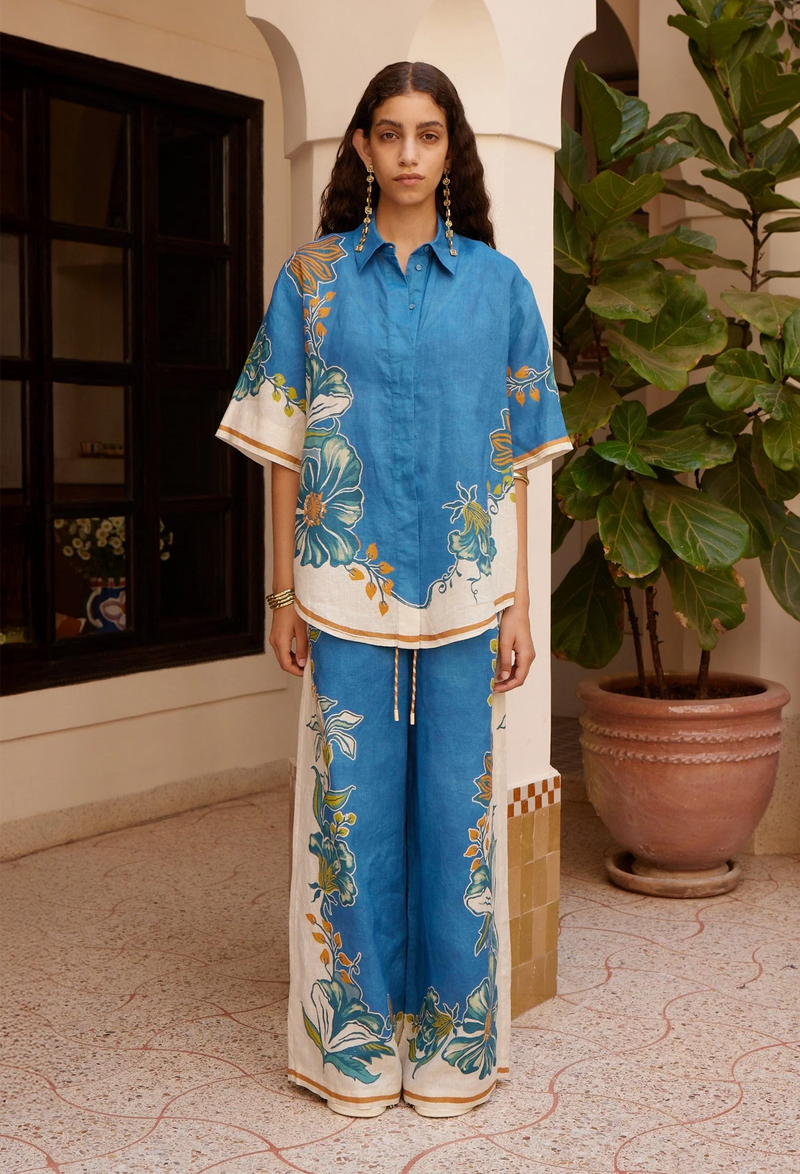 Woman wearing a blue floral outfit standing in front of a building with a plant.