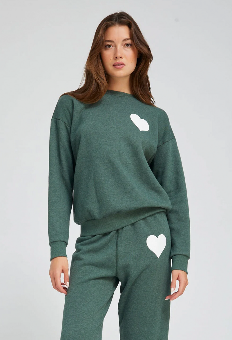 Woman wearing a green sweatshirt and pants with white heart designs on a light gray background