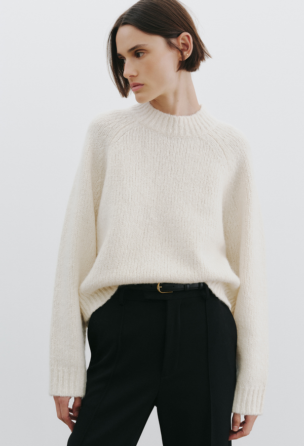 woman wearing an off white knit sweater and pants on a white background