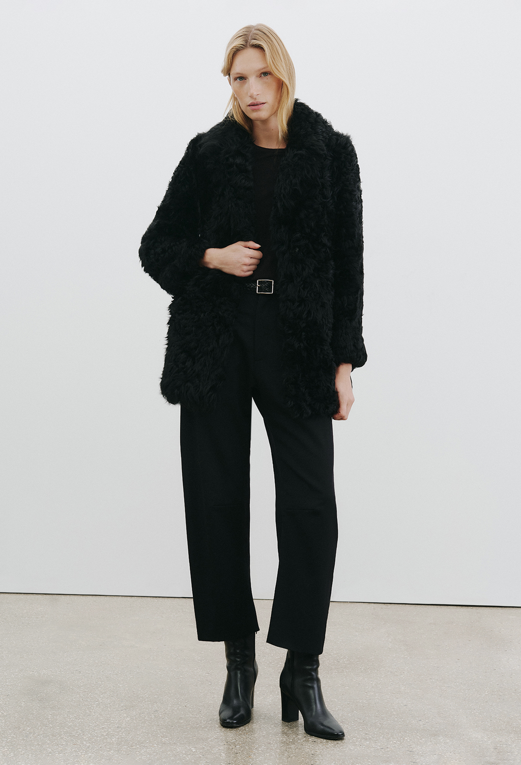 a woman wearing a black coat and black pants on a white background