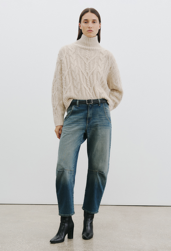 woman wearing a light beige chunky knit sweater and jeans on a white background