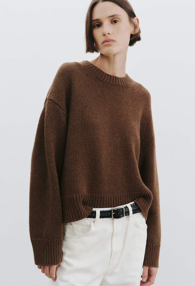 woman wearing a brown sweater and jeans on a white background