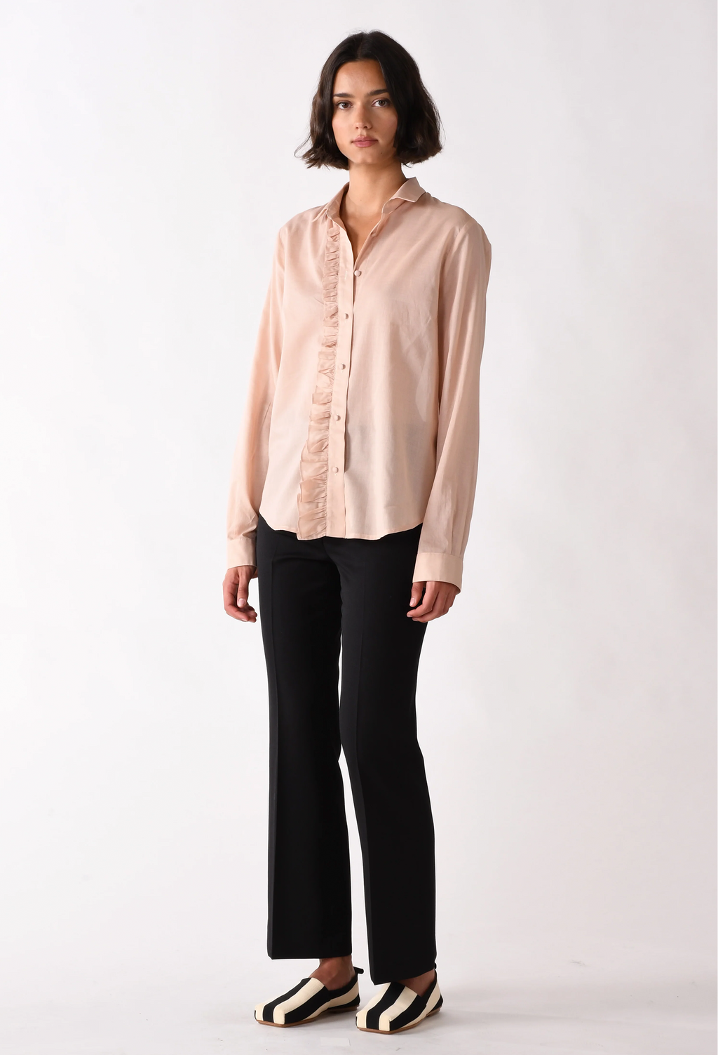 Woman wearing a light pink blouse and black pants on a white background