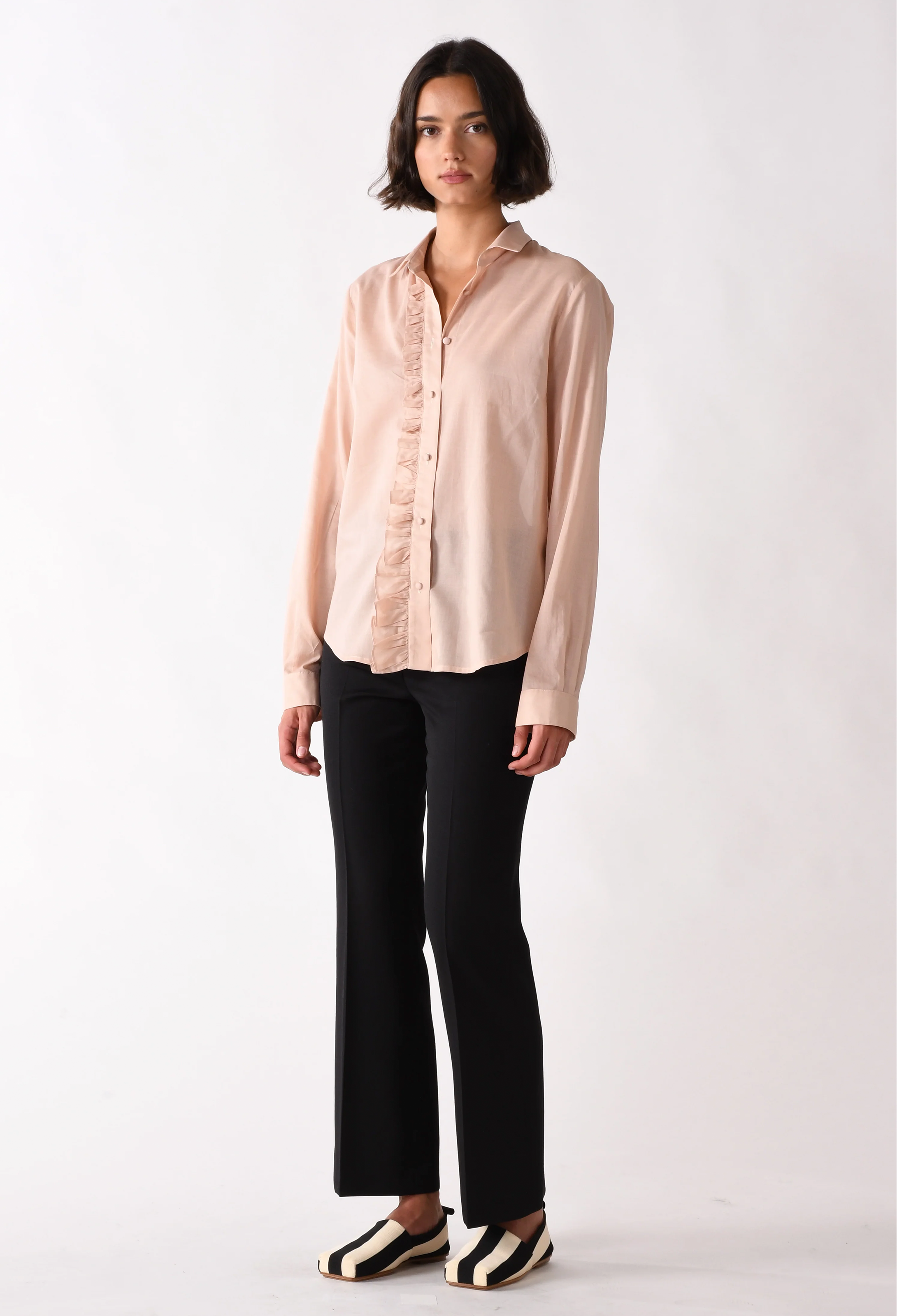 Woman wearing a light pink blouse and black pants on a white background