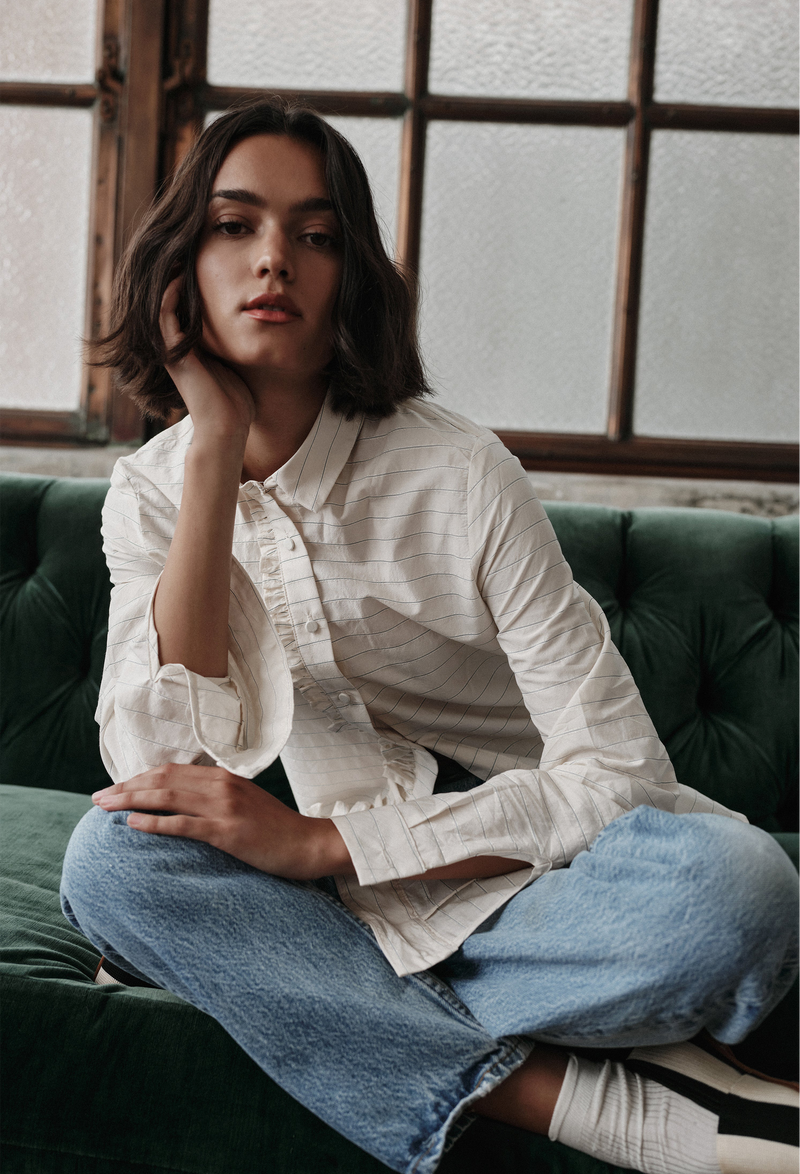Woman sitting on a green couch wearing a white shirt and blue jeans, with a window in the background.