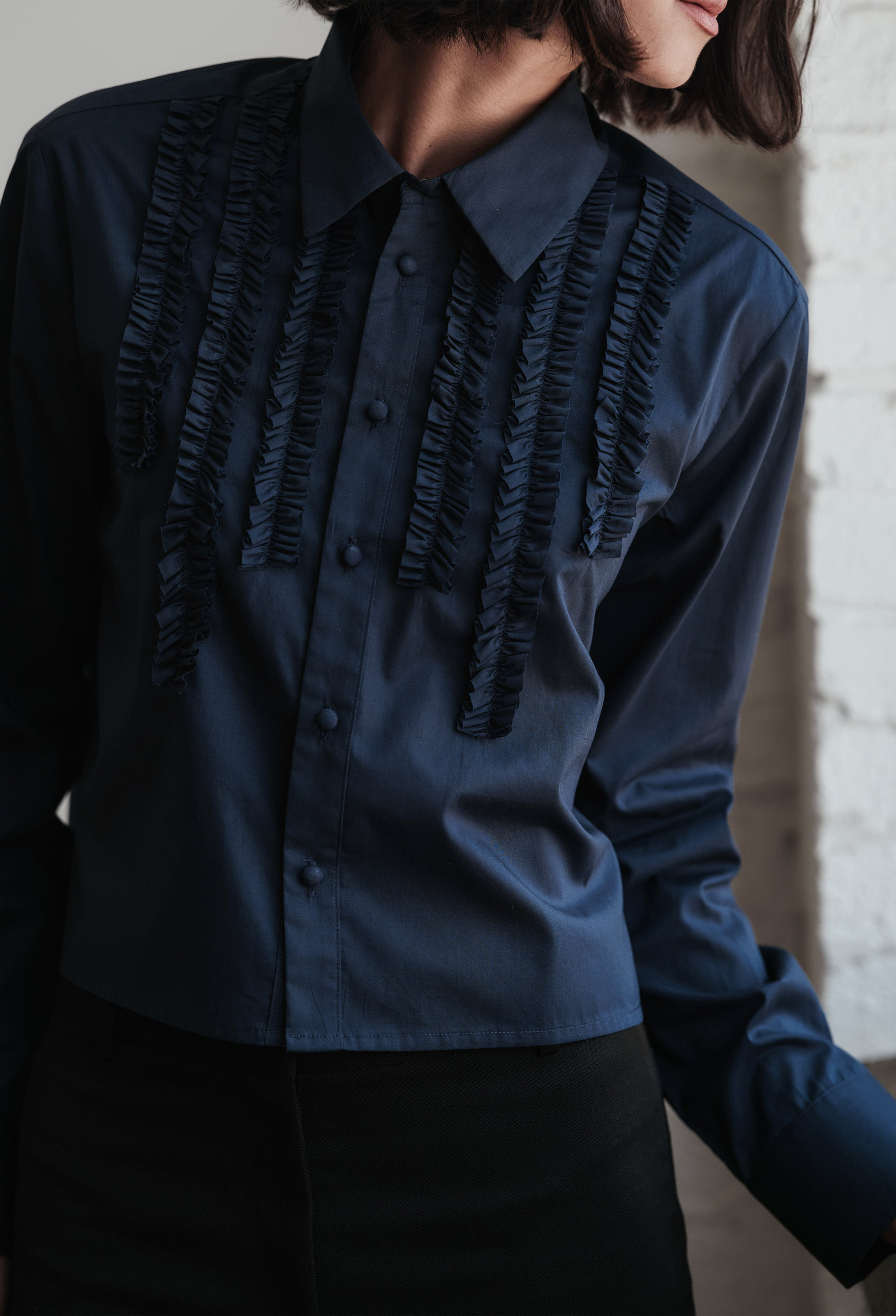 Navy blue shirt with ruffled details worn by a person against a neutral background
