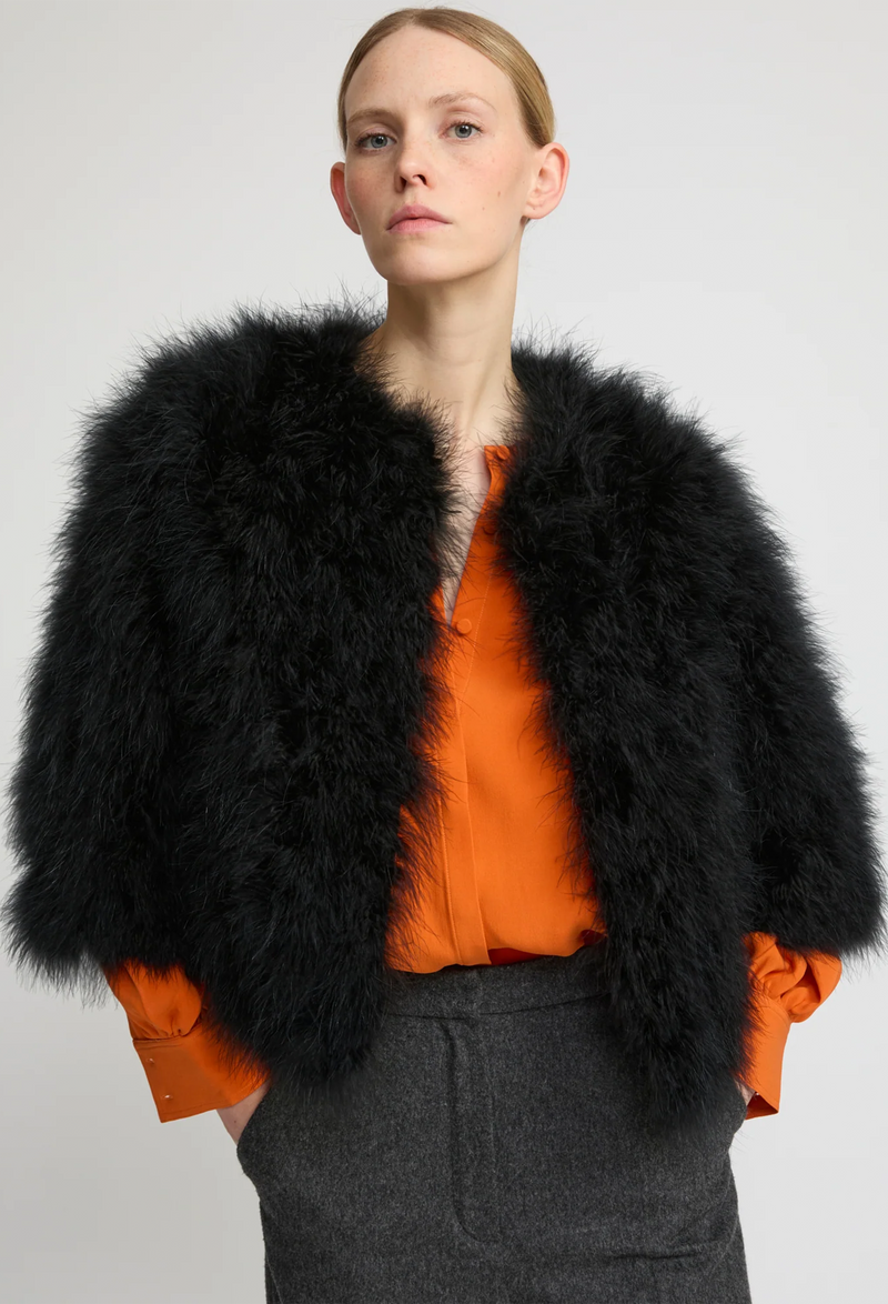 Person wearing a black feathered jacket over an orange top on a plain background