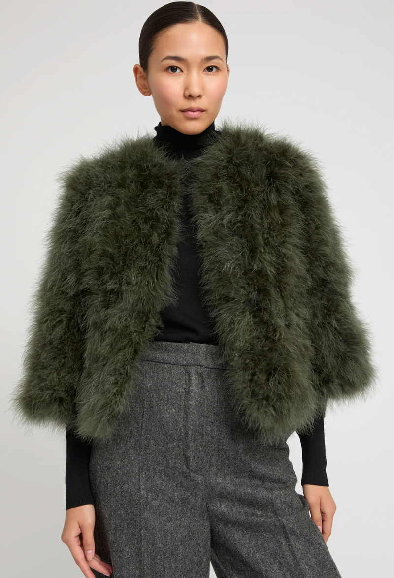 Woman wearing a green feathered shrug over a black top and gray pants on a white background