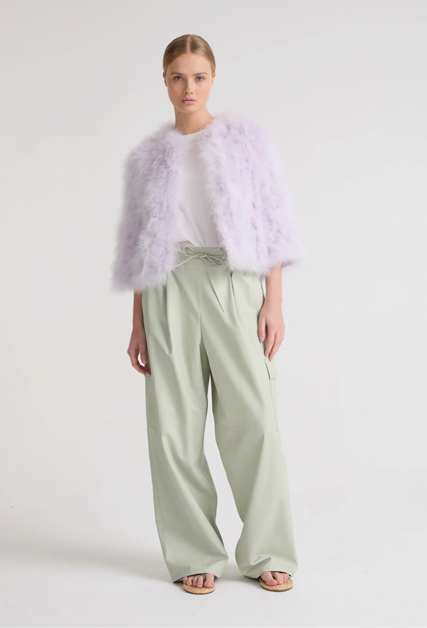 Woman wearing a light purple fur vest over a white top and light green pants on a white background