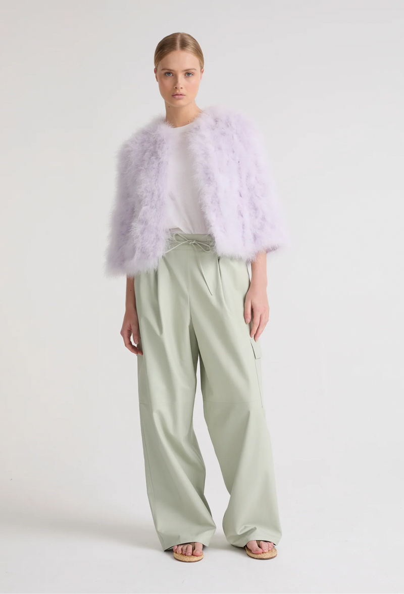 Woman wearing a light purple fur vest over a white top and light green pants on a white background