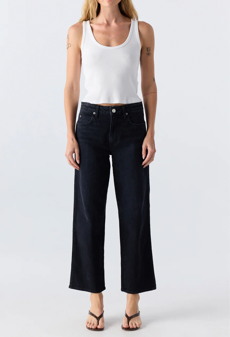 Person wearing a white tank top and black jeans on a light gray background