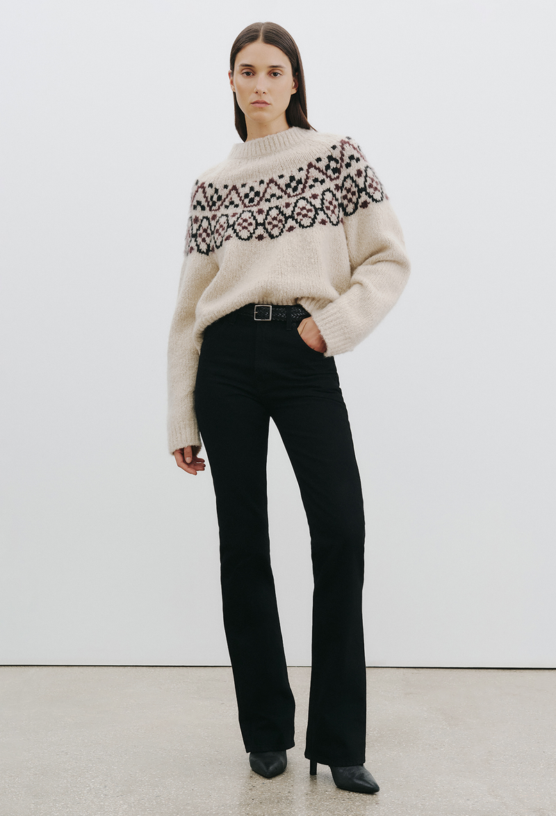 Woman wearing a beige fair isle sweater with a plain background