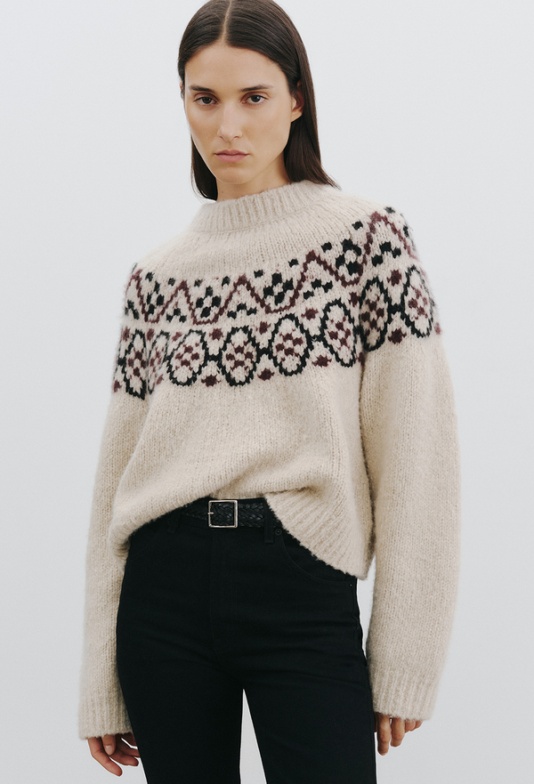 Woman wearing a beige fair isle sweater with a plain background