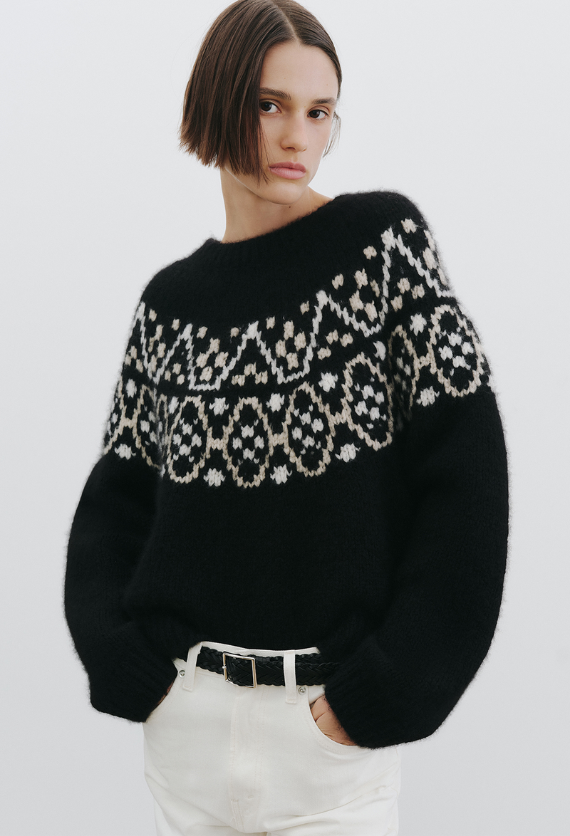 Person wearing a black sweater with fair isle pattern on a plain background
