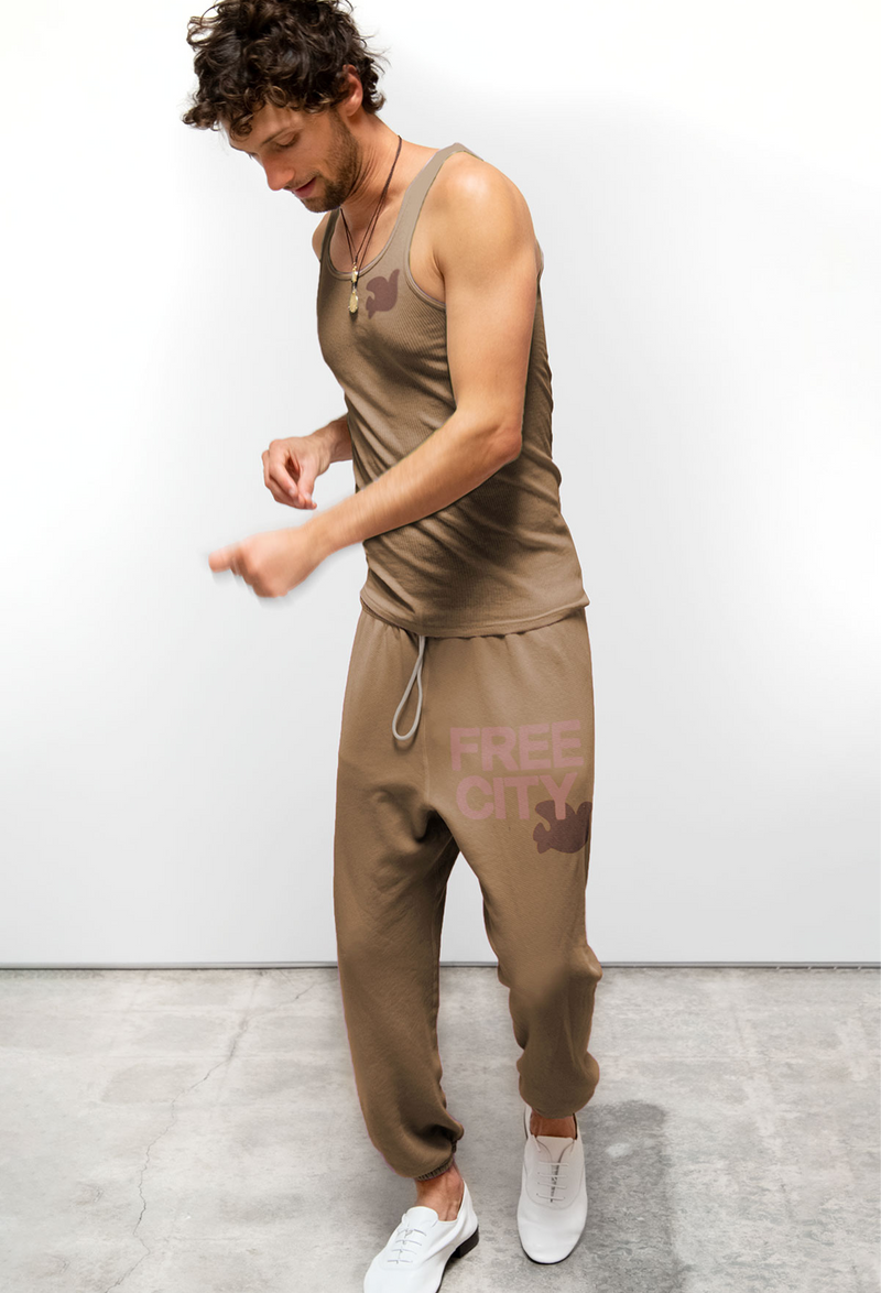 Man wearing a brown tank top and pants with 'Free City' branding against a white background