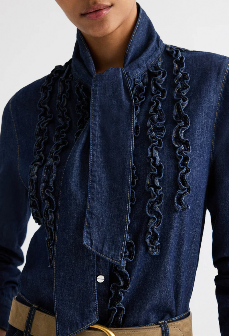 Blue denim top with ruffled details on a plain background
