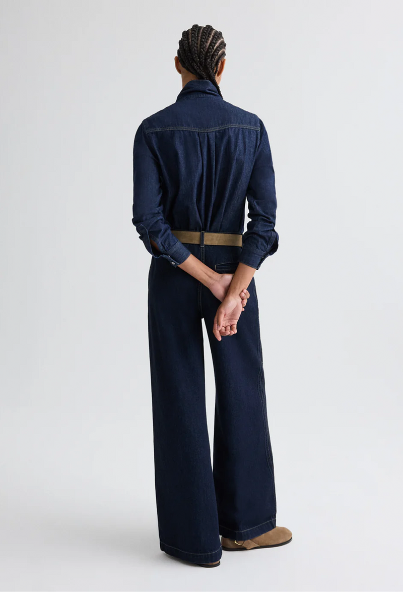 Person wearing a dark denim outfit with wide-leg jeans on a white background