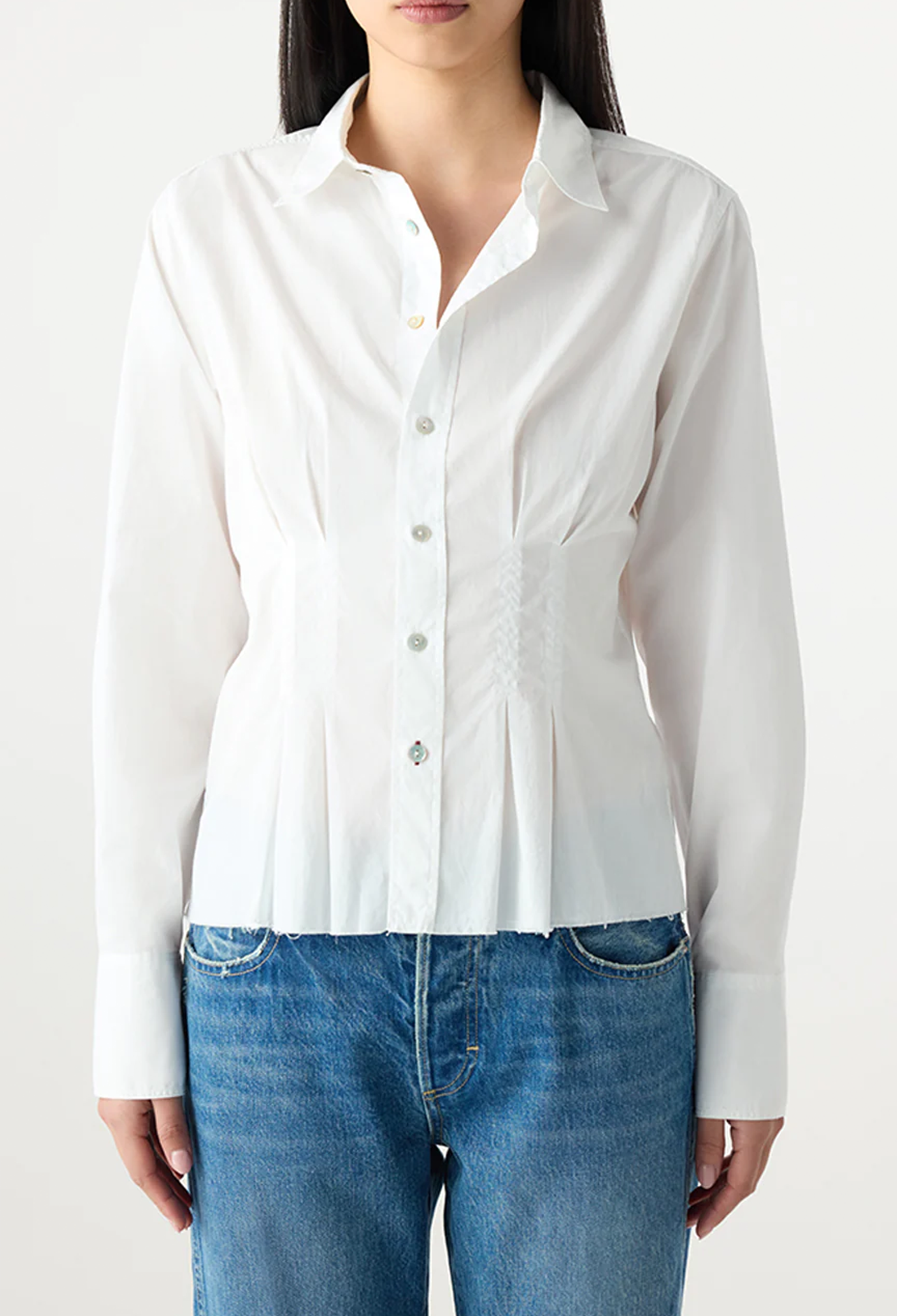Person wearing a white button-up shirt and blue jeans on a plain background