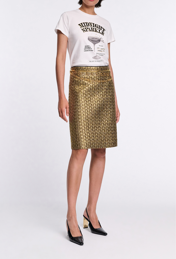 Person wearing a white t-shirt with text and a gold patterned skirt on a white background