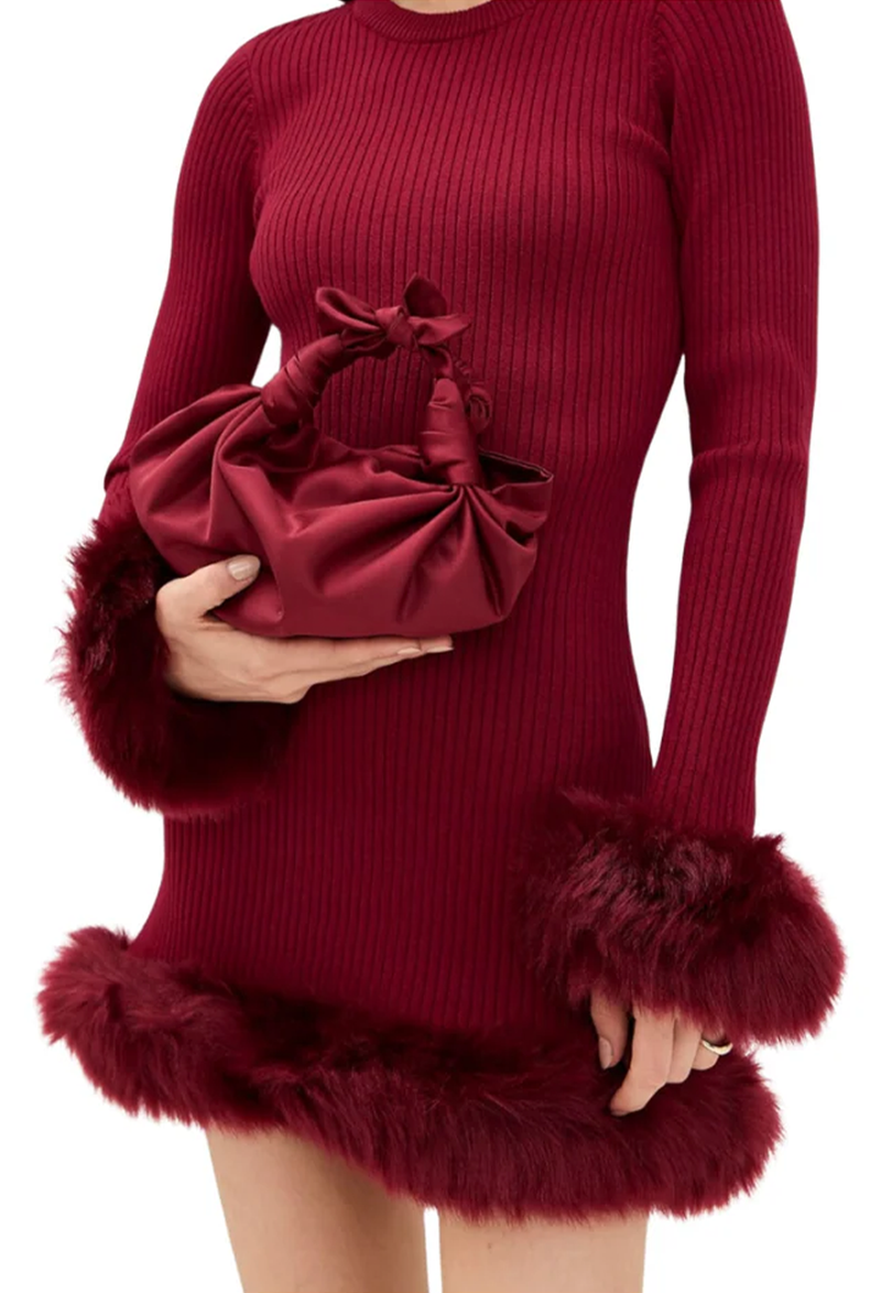 Person wearing a burgundy ribbed dress with fur-trimmed cuffs holding a matching clutch.