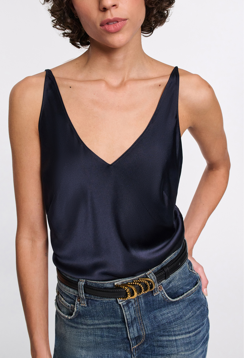 a woman wearing a dark navy v-neck silk camisole and jeans on a white background
