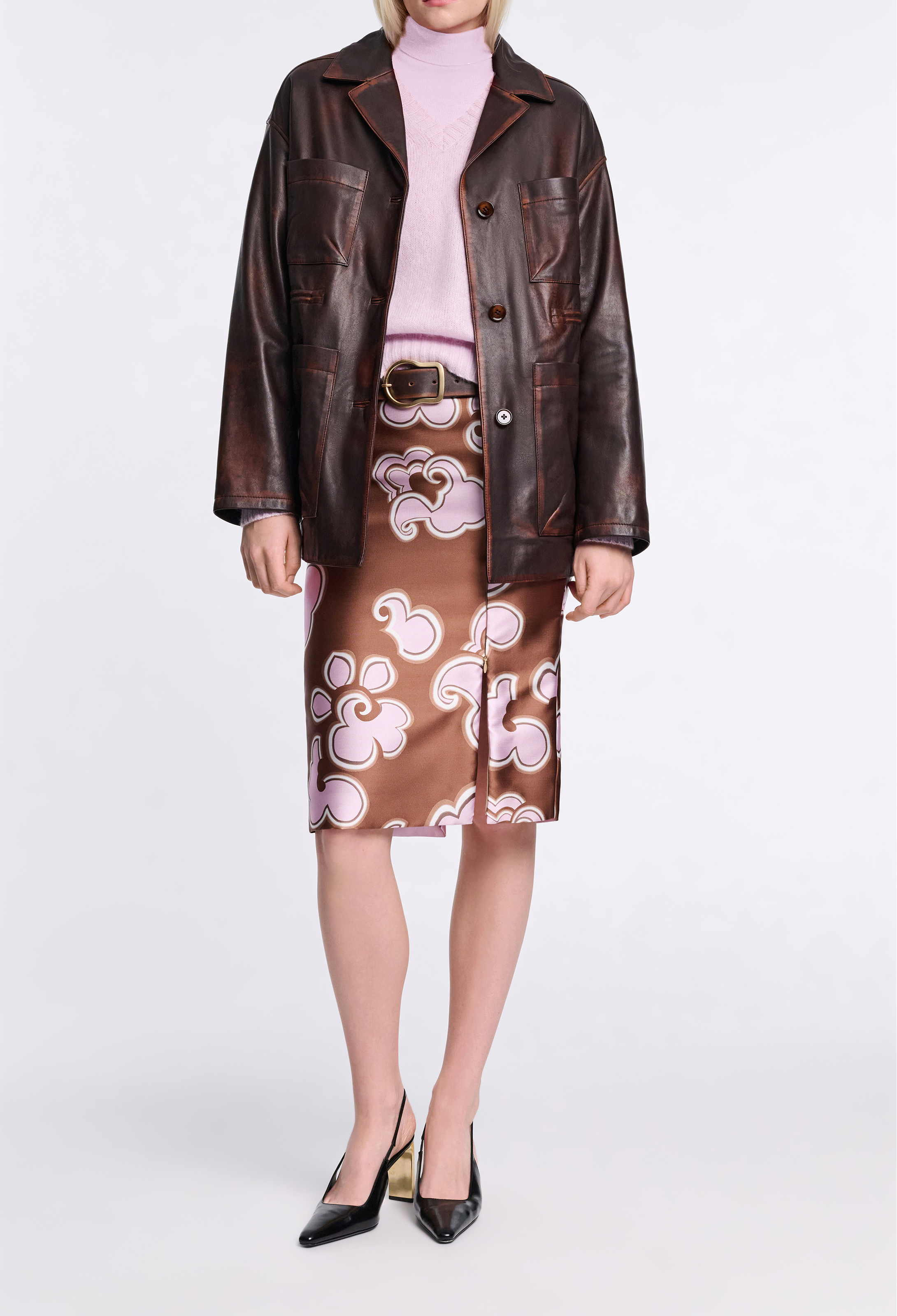 Person wearing a brown leather jacket and brown and pink patterned skirt on a white background