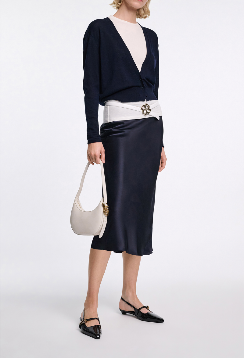 a woman wearing a dark navy v-neck cardigan and silk skirt on a white background