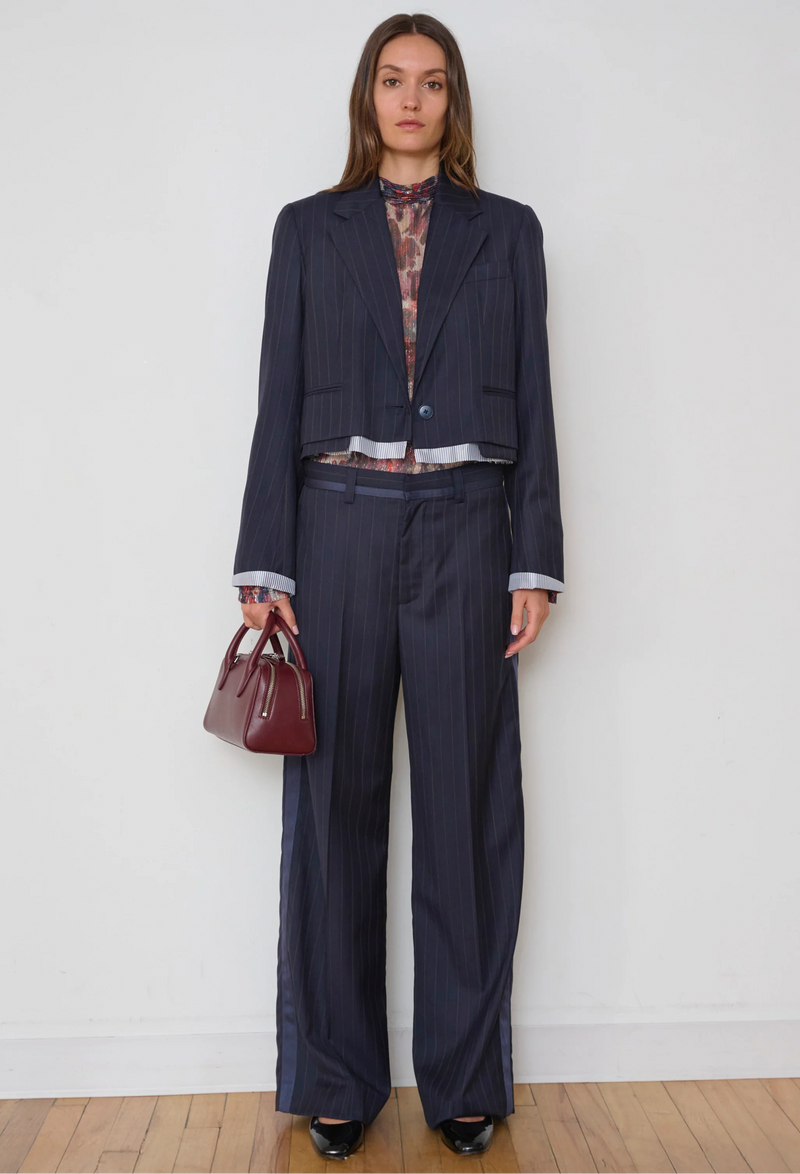 Woman wearing a navy suit holding a red handbag against a white background