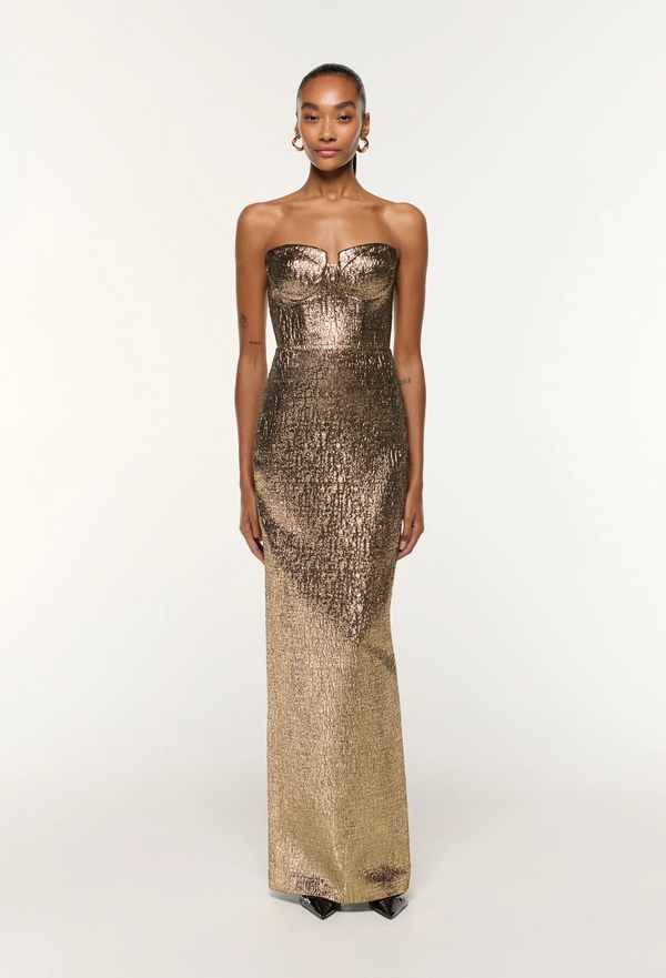 Woman wearing a strapless, long, metallic gold dress on a white background
