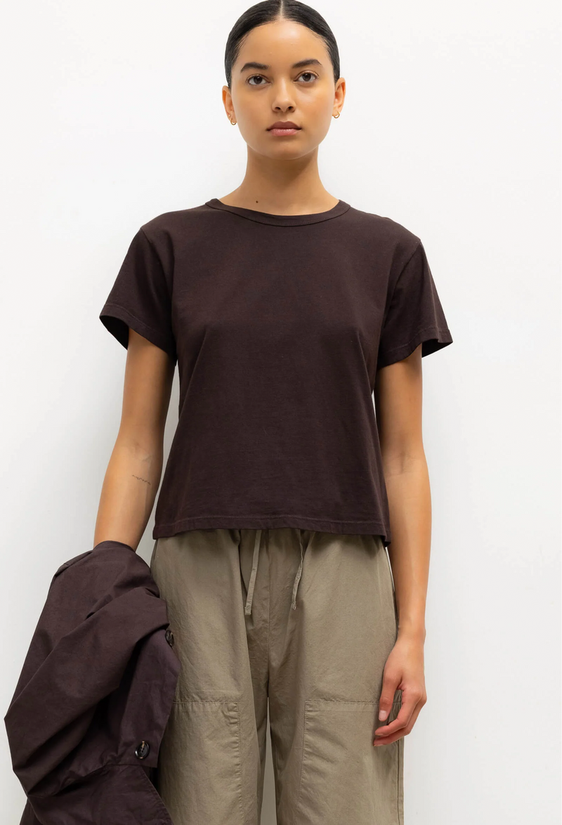 Person wearing a brown t-shirt and beige pants against a white background