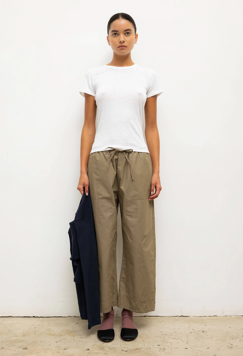 Person wearing a white t-shirt and beige pants holding a black jacket against a white background