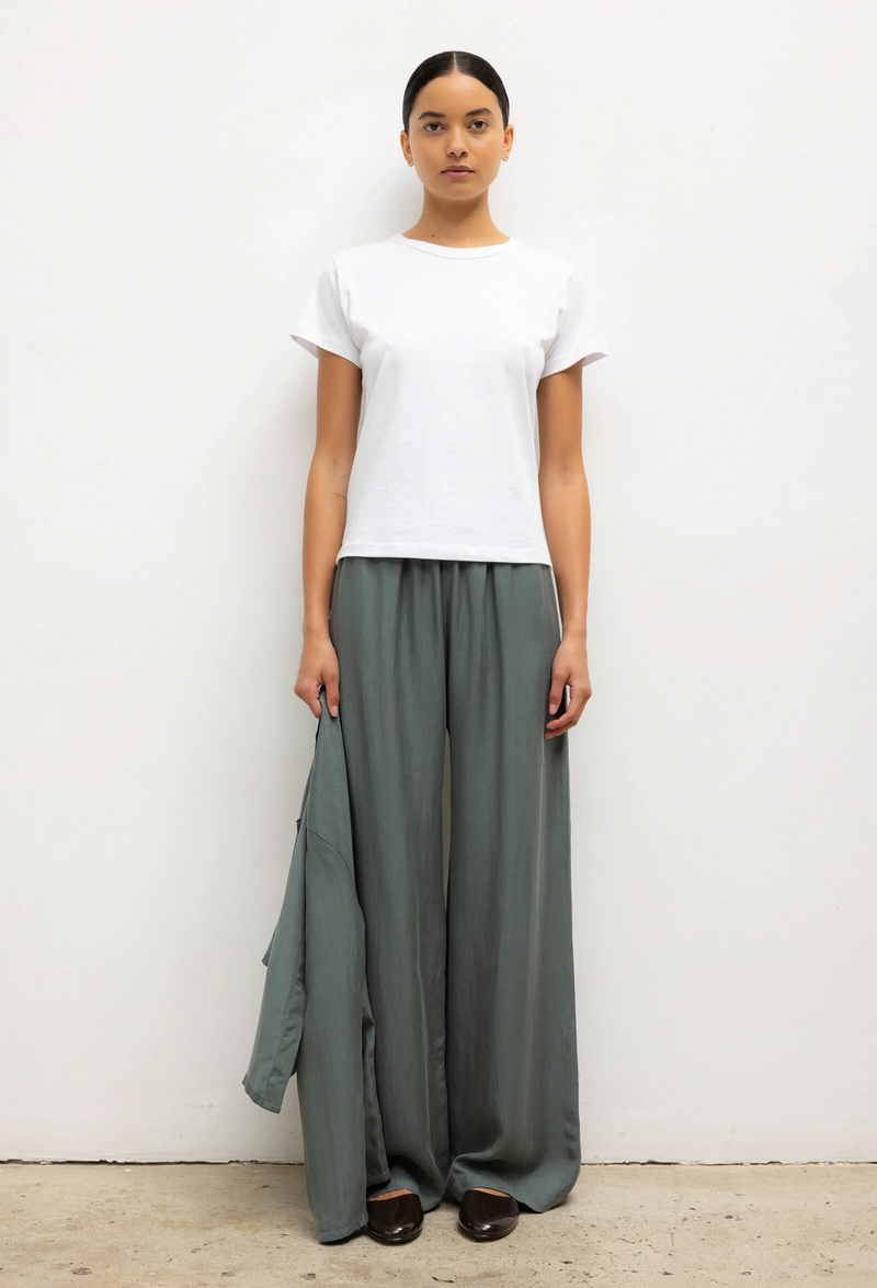 Woman wearing a white top and green wide-leg pants against a white background