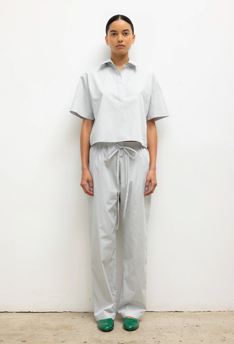 Person wearing a light striped shirt and pants standing against a white wall.