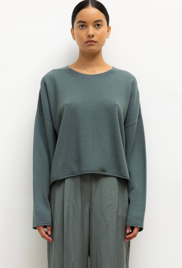 Person wearing a teal sweater and pants against a white background